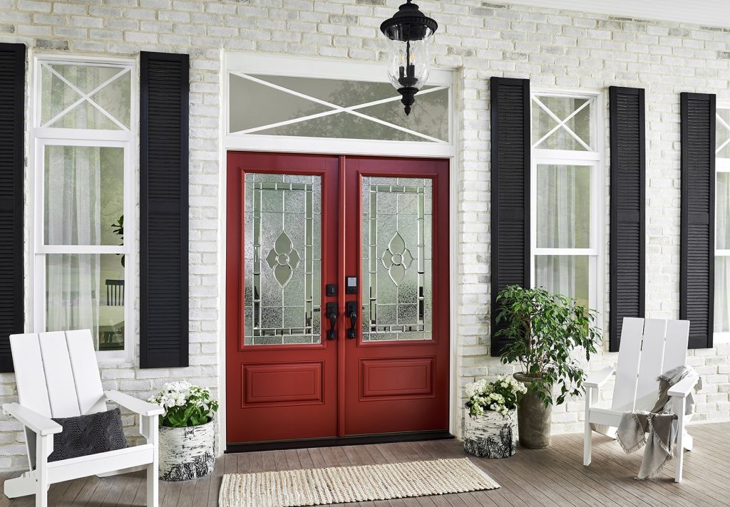 A bright red front entry door accompanied by white porch chairs and potted plants.